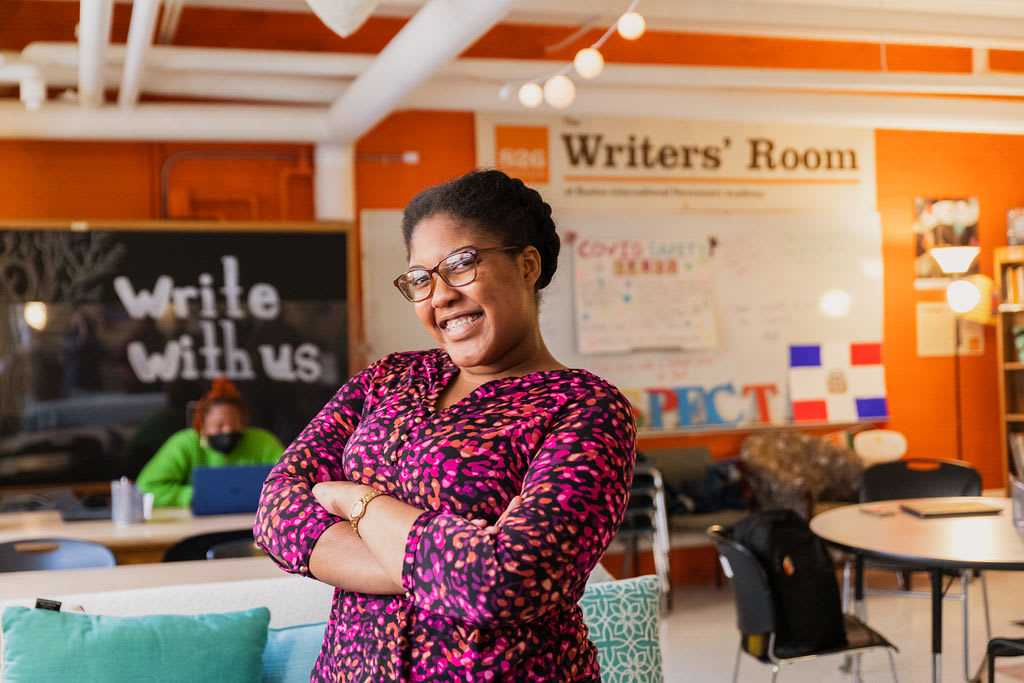 A student faces the camera with a smile. She is in the Writers' Room of a school. 