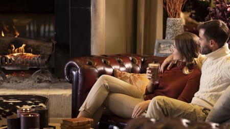 Couple buvant un chocolat chaud sur le canapé du salon de l'Hôtel Ermitage devant la cheminée.