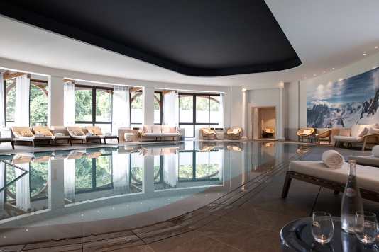Piscine intérieure de l'EVIANSPA de l'Hôtel Royal avec des fauteuils et transats de long de la piscine