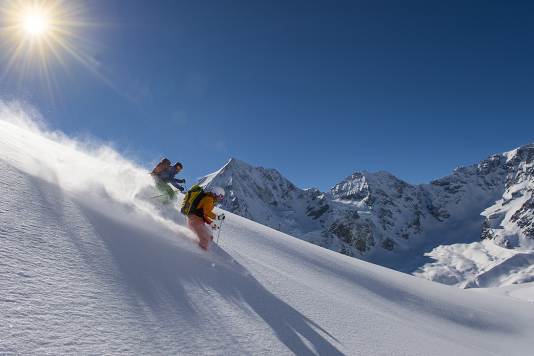 Deux skieurs en descente avec le soleil et les montagnes à l'arrière