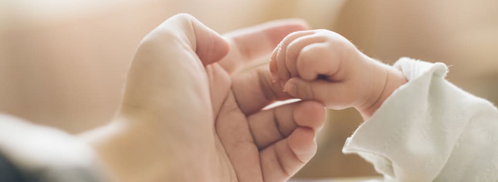une main d'adulte tenant une petite main de bébé pour le programme Maman & Bébé de l'Hôtel Royal