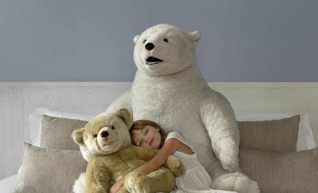petite fille sur un lit avec deux grosses peluches ours