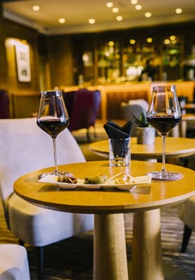 Deux verres de vins rouge et des amuses-bouches posés sur une table du Bar La Bibliothèque de l'Hôtel Ermitage