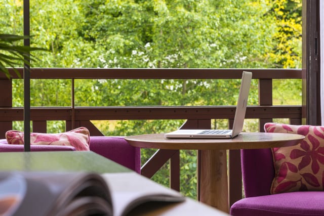 Vue du salon de la chambre Deluxe Sud à l'Hôtel Ertmiage avec un ordinateur posé sur la table et vue sur le parc