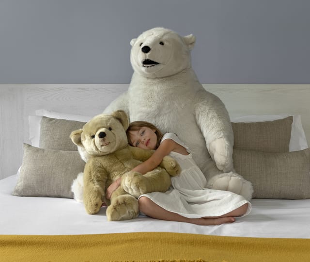 petite fille sur un lit avec deux grosses peluches ours