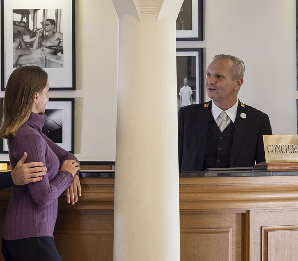 Une femme de dos demandant des conseils au concierge de l'Hôtel Royal
