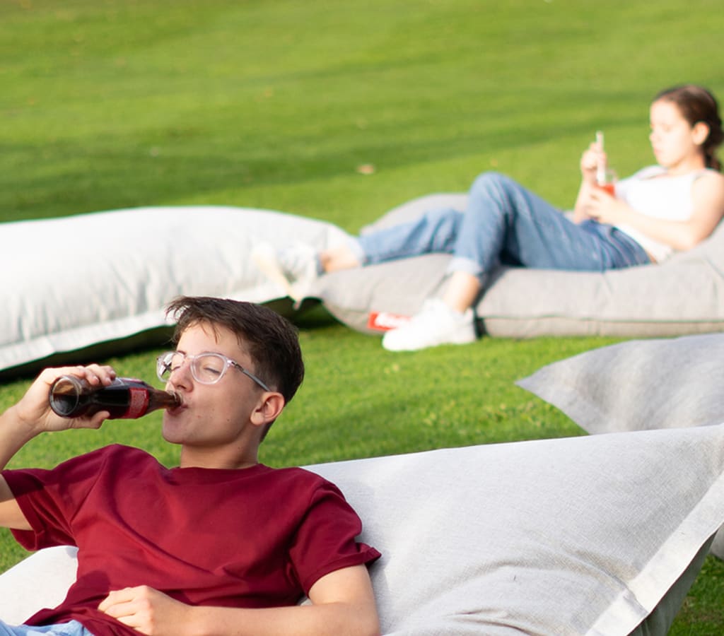 Drei junge Leute auf Fatboys in der Sonne und trinken ihre Getränke