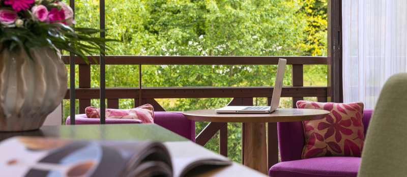 Vue du salon de la chambre Deluxe Sud à l'Hôtel Ertmiage avec un ordinateur posé sur la table et vue sur le parc