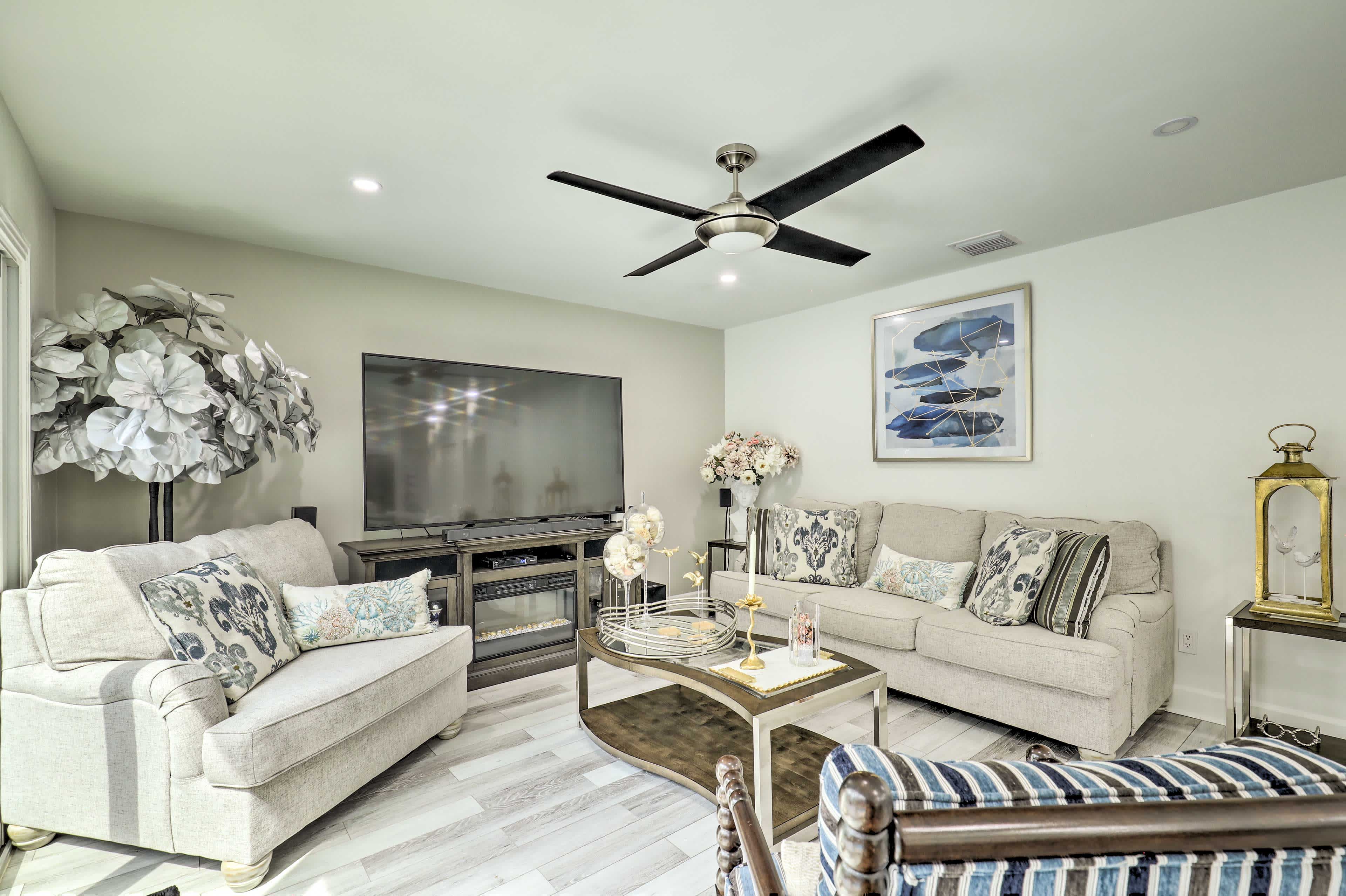 light colored interior room with a couch and chairs with pattered throw pillows and a large tv with muted colored flowers in the corners of the room