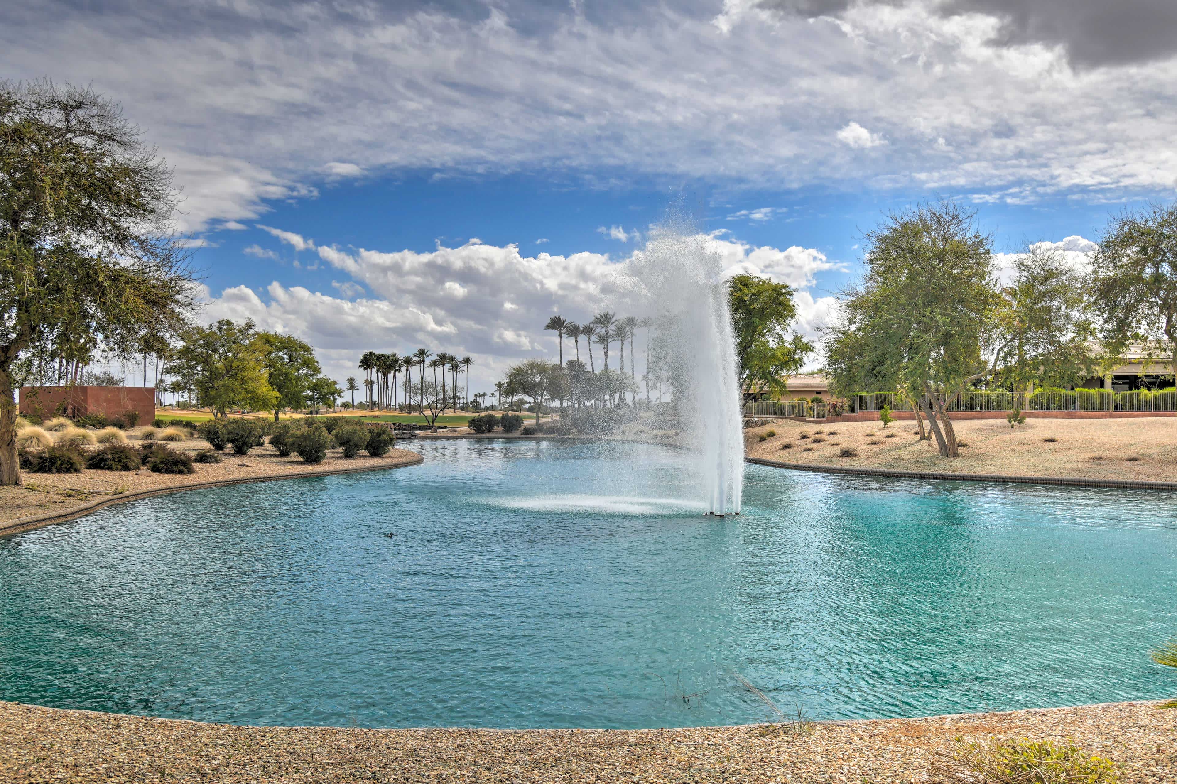 View of a small pond and water fountain surrounded by green trees in Surprise, AZ