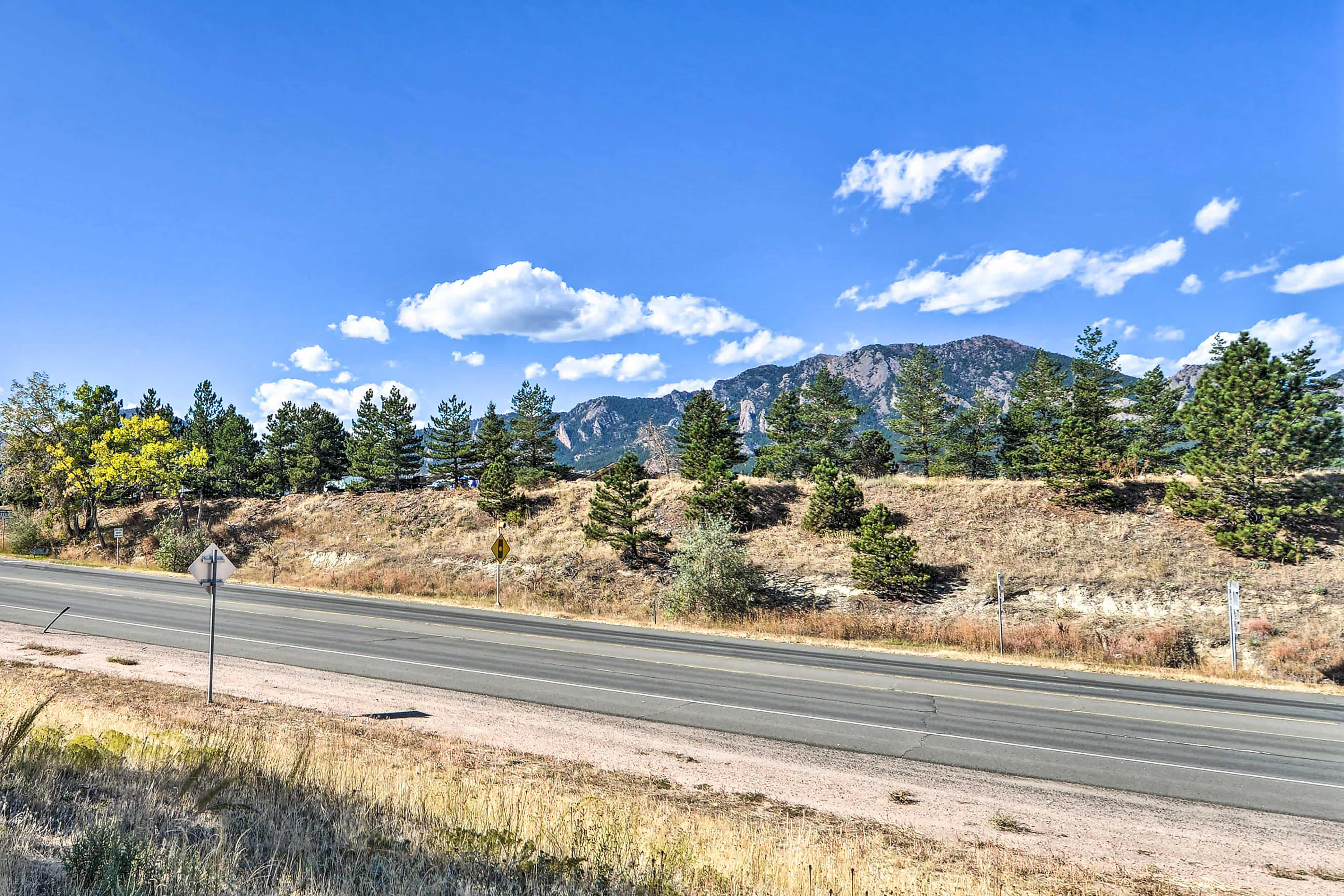 View of the mountains in Boulder, CO with trees and a street in the foreground and blue sky overhead