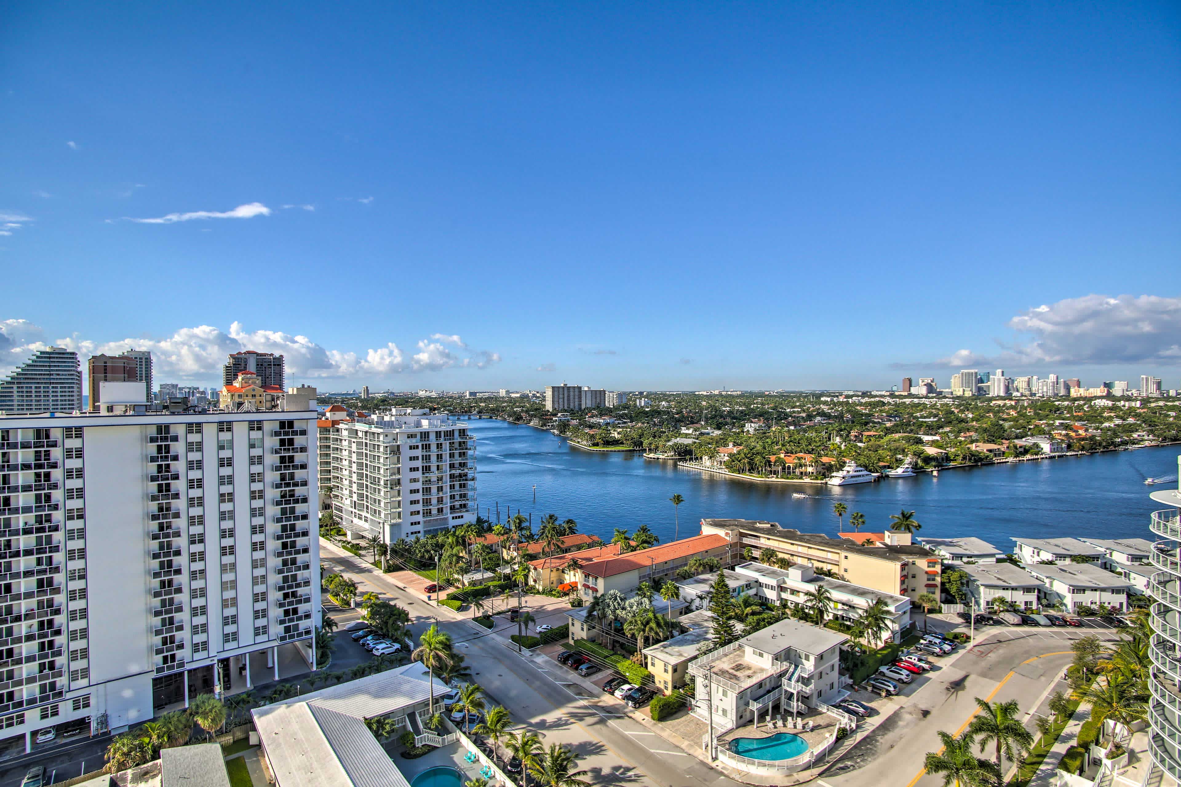 Aerial view of Fort Lauderdale, FL overlooking buildings, palm trees, and a blue river and blue skies