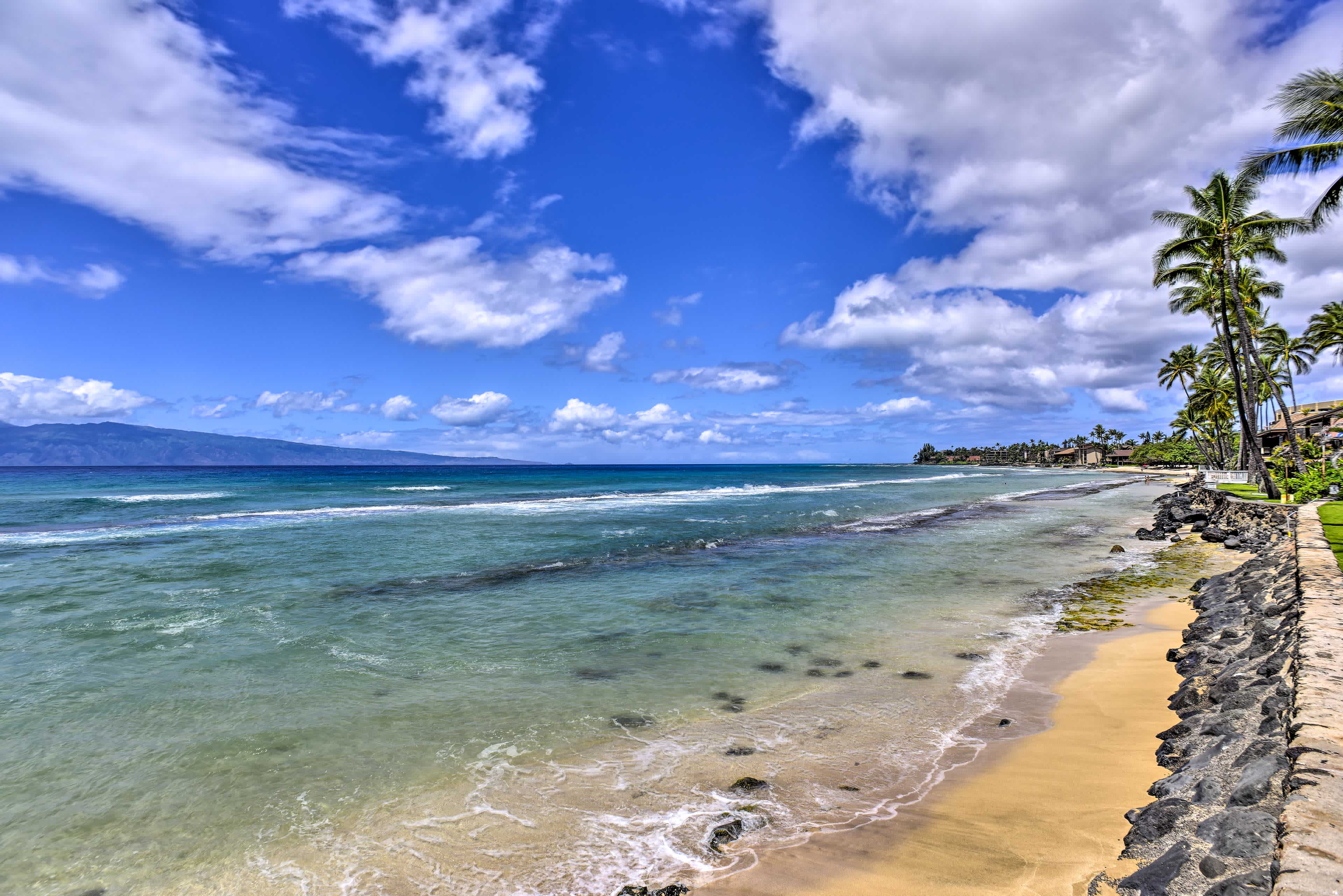 View of a shoreline and beach with blue water, blue skies, and a distant island in Lahaina, HI