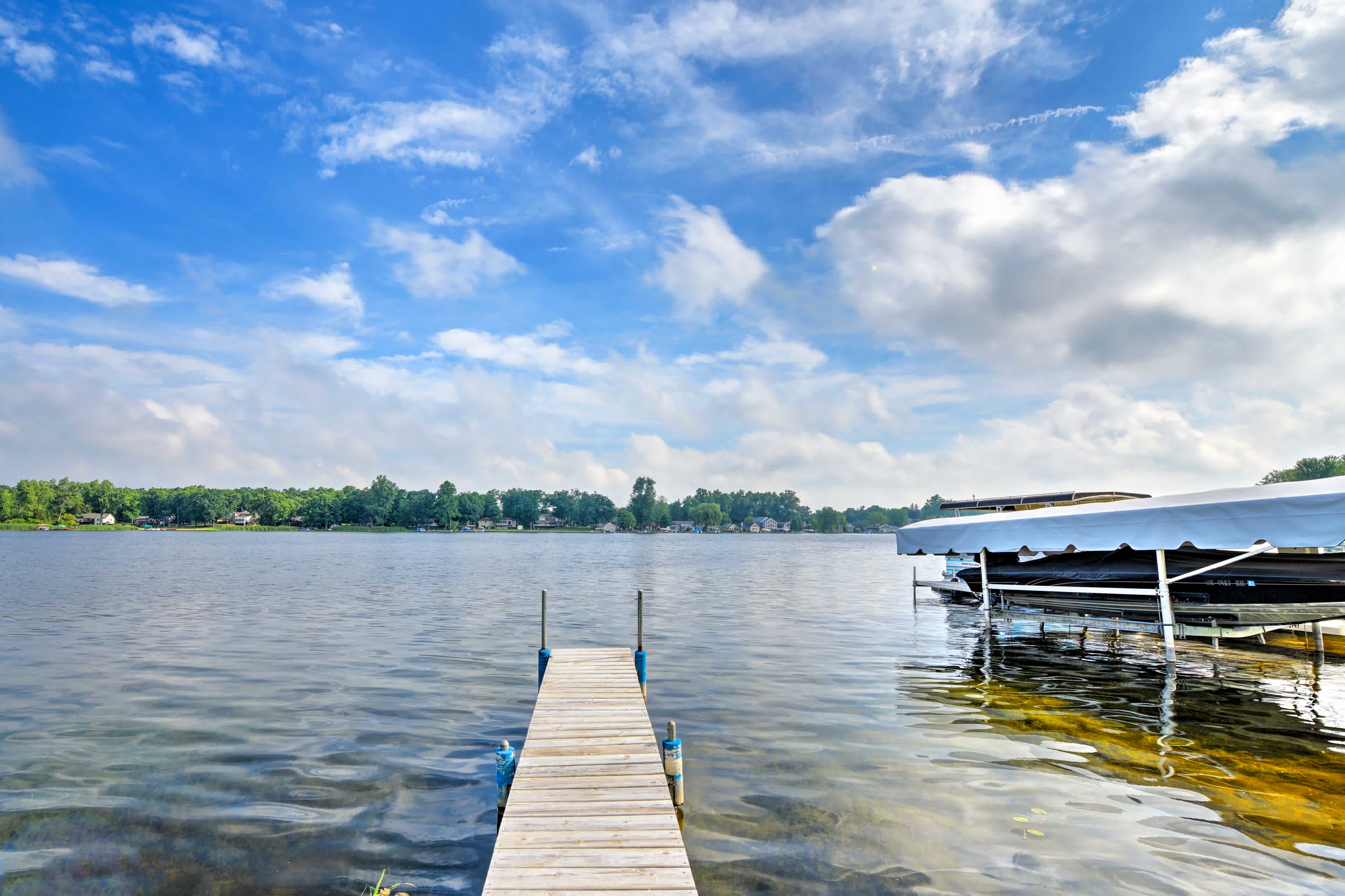 View from a wooden dock overlooking an inland lake in Jackson, MI with a boat on a lift on the right, and blue skies overhead