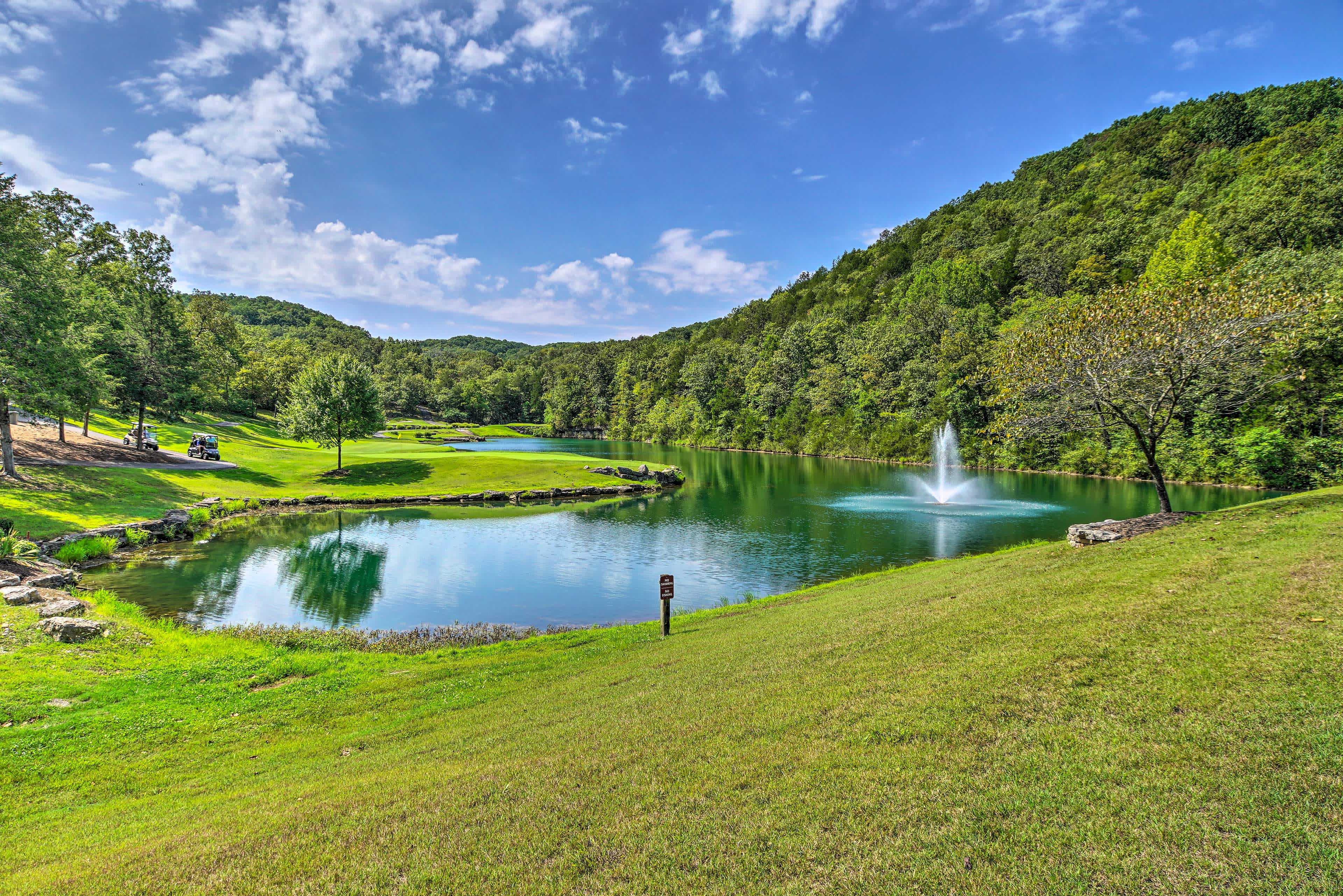 View of a pond with a fountain and tree-covered hills in Branson West, MO