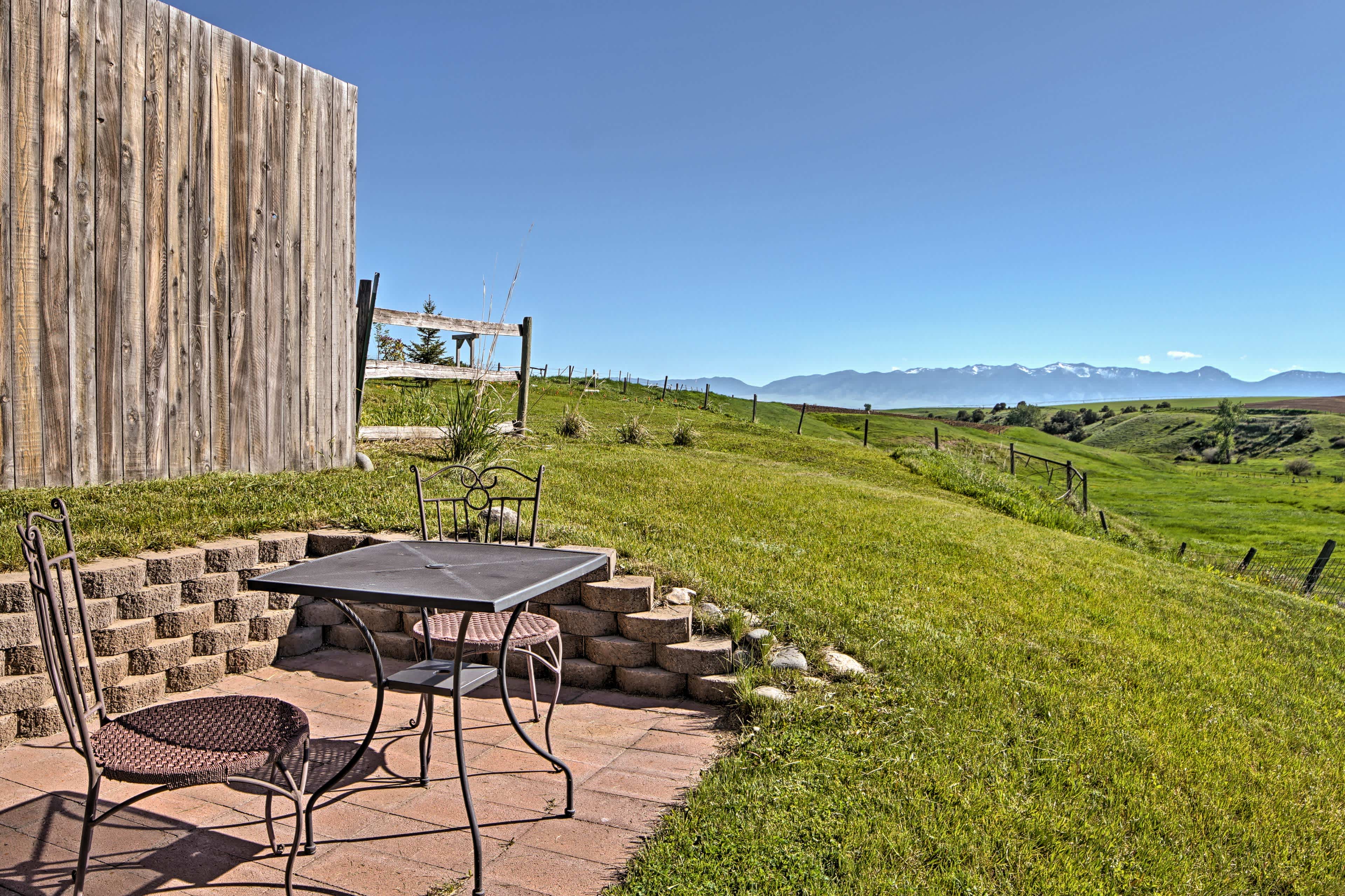 View of a green field in Bozeman, MT with distant mountains on the right side and a small table for two people on the left