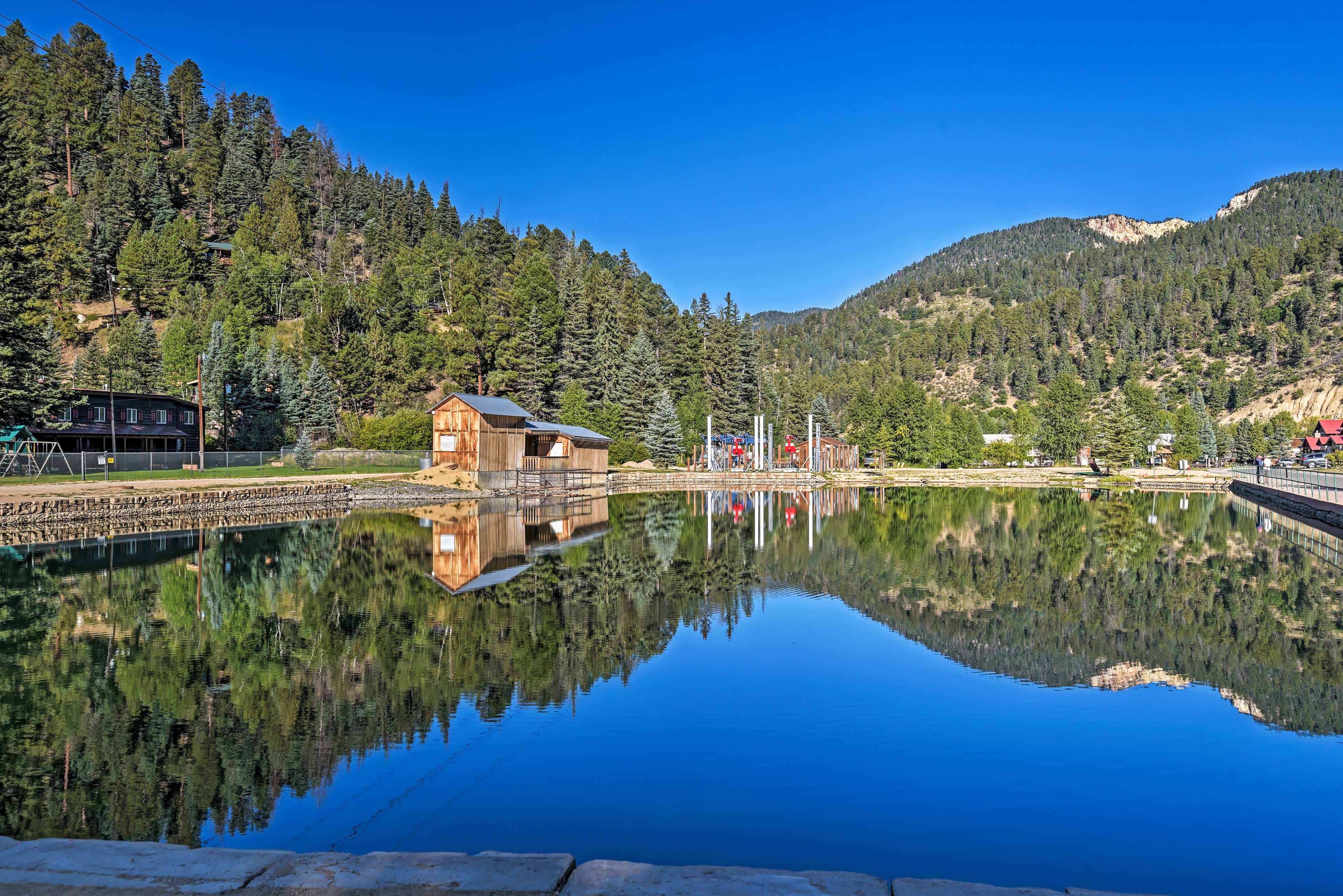 View of mountains in the background and a small pond in the foreground with blue skies overhead in Red River, NM