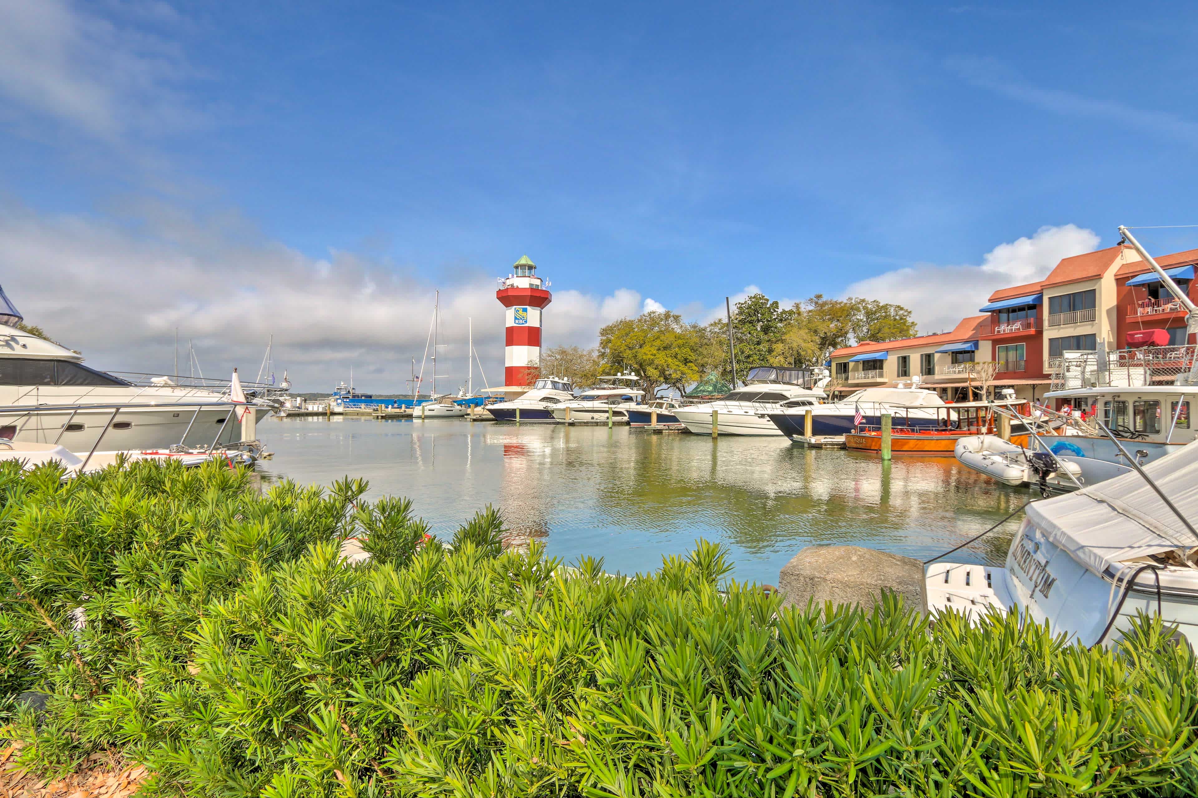 Canal in Hilton Head Island, SC with greenery in the foreground, and boats in the canal with a lighthouse in the background and blue sky overhead