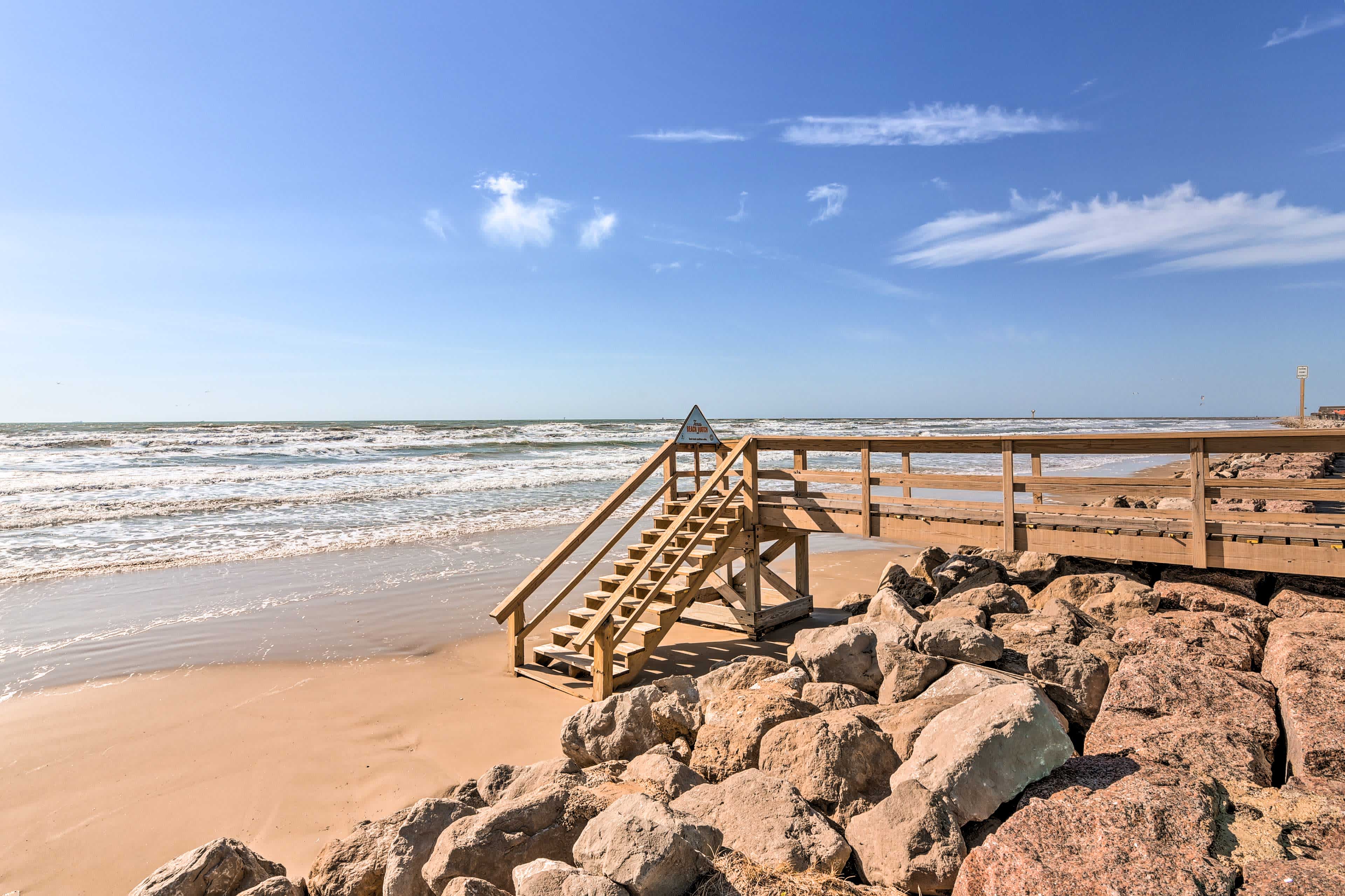 View of a beach in Freeport, TX with rocks and a wooden walkway on the right side