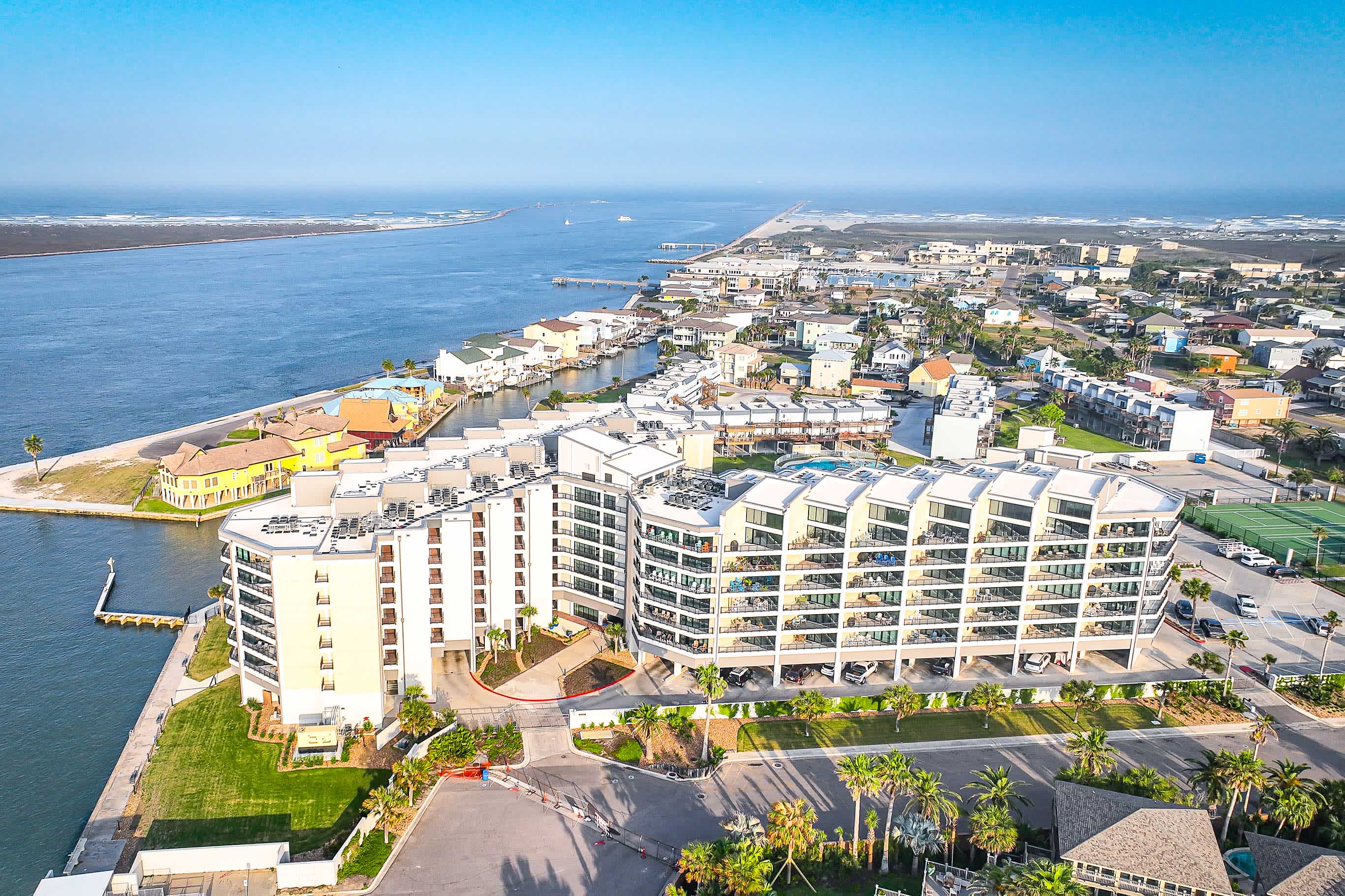 Drone photo of Port Aransas, TX with buildings and condos on the right and water on the left with blue skies above