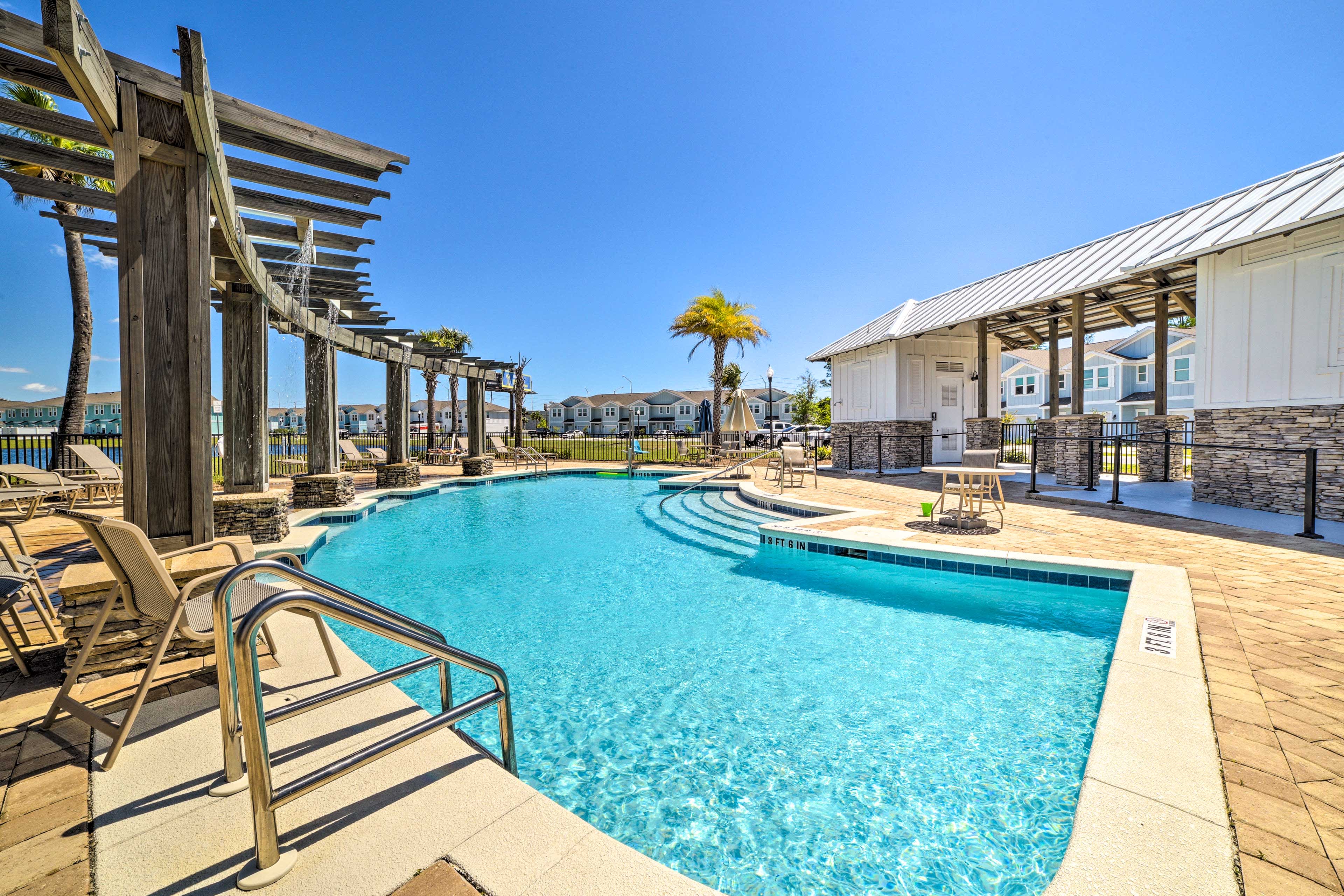 Community pool surrounded by lounge chairs and tables with blue skies above