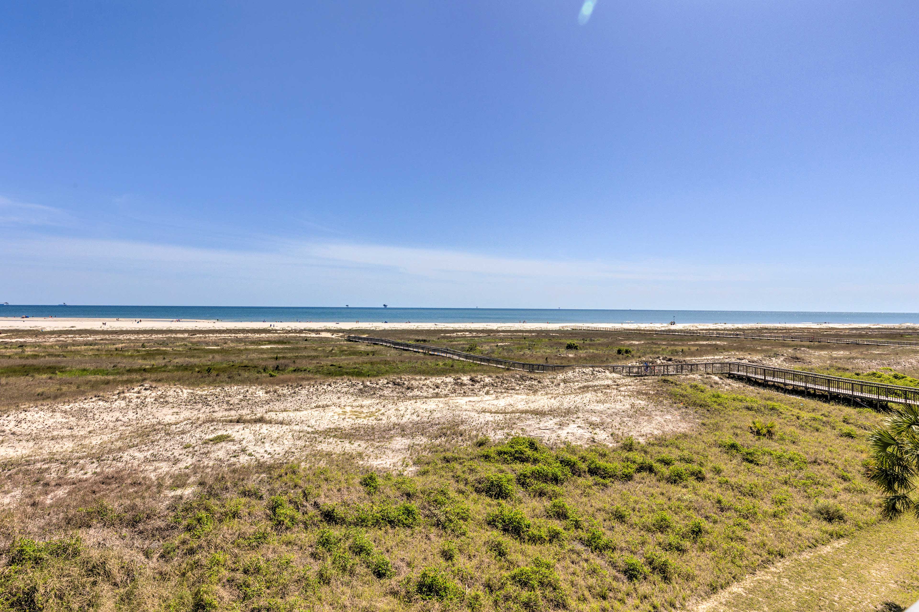 View of green grasses with a long wooden dock leading through the grass to the ocean