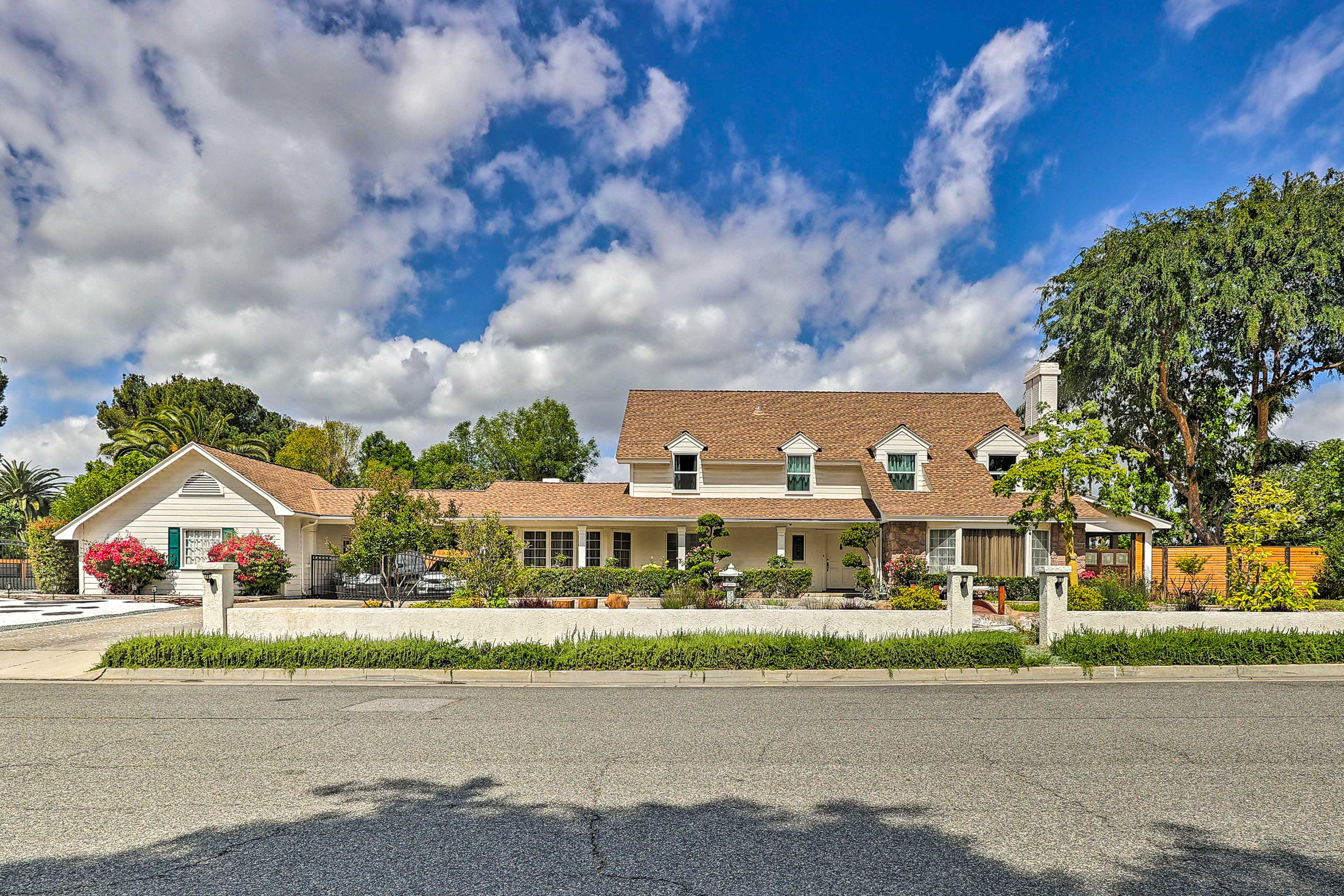 Straight-on view of a generic home with brown roof, green trees, and a blue cloudy sky