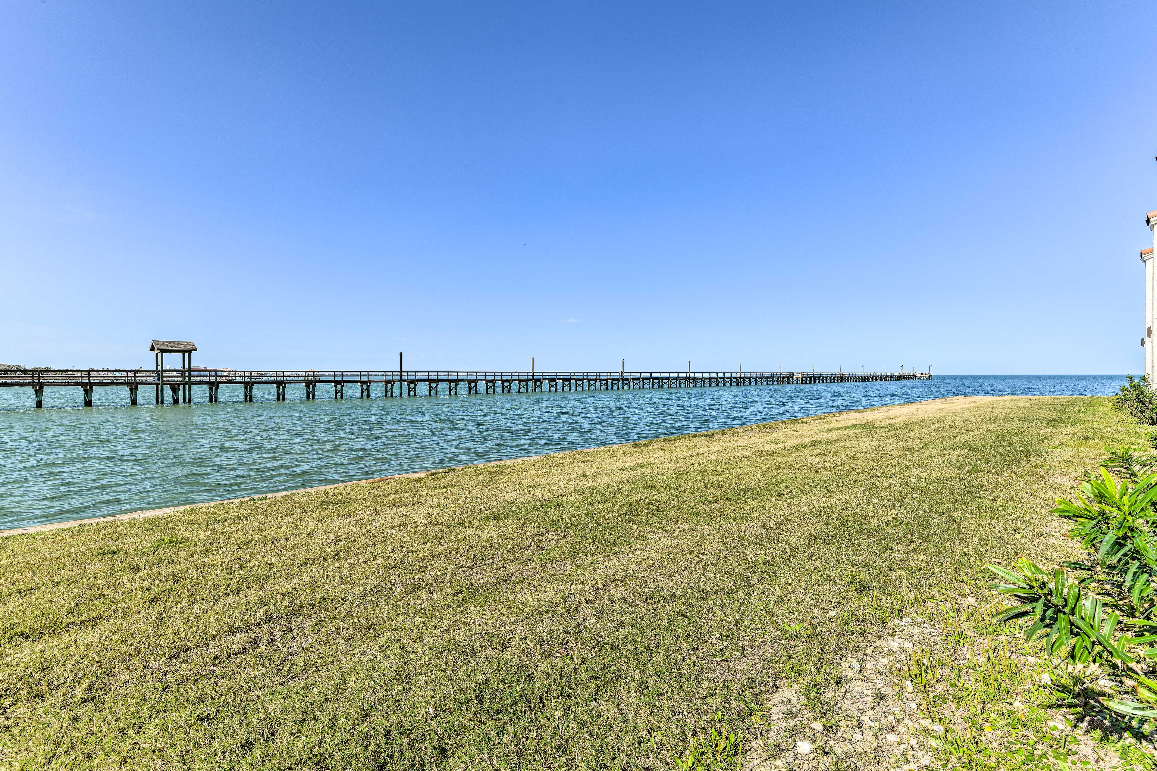 Blue skies in Rockport, TX with green grass in the foreground and a pier in the water through the center
