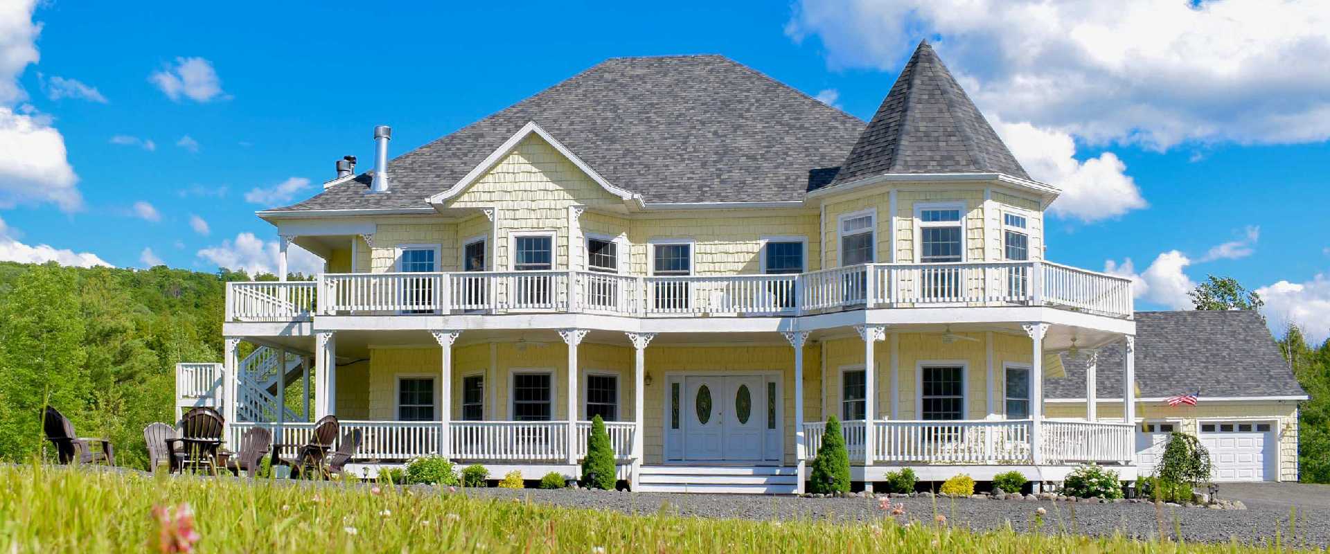 Photo of the exterior of a Victorian manor vacation rental near Windham, New York. The photo is taken during summer with lush trees and greenery.