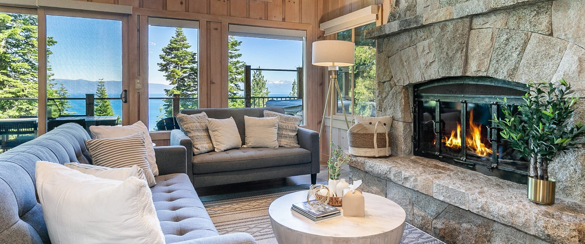 Cabin living room with a roaring fire in a large stone fireplace, overlooking the mountains and water