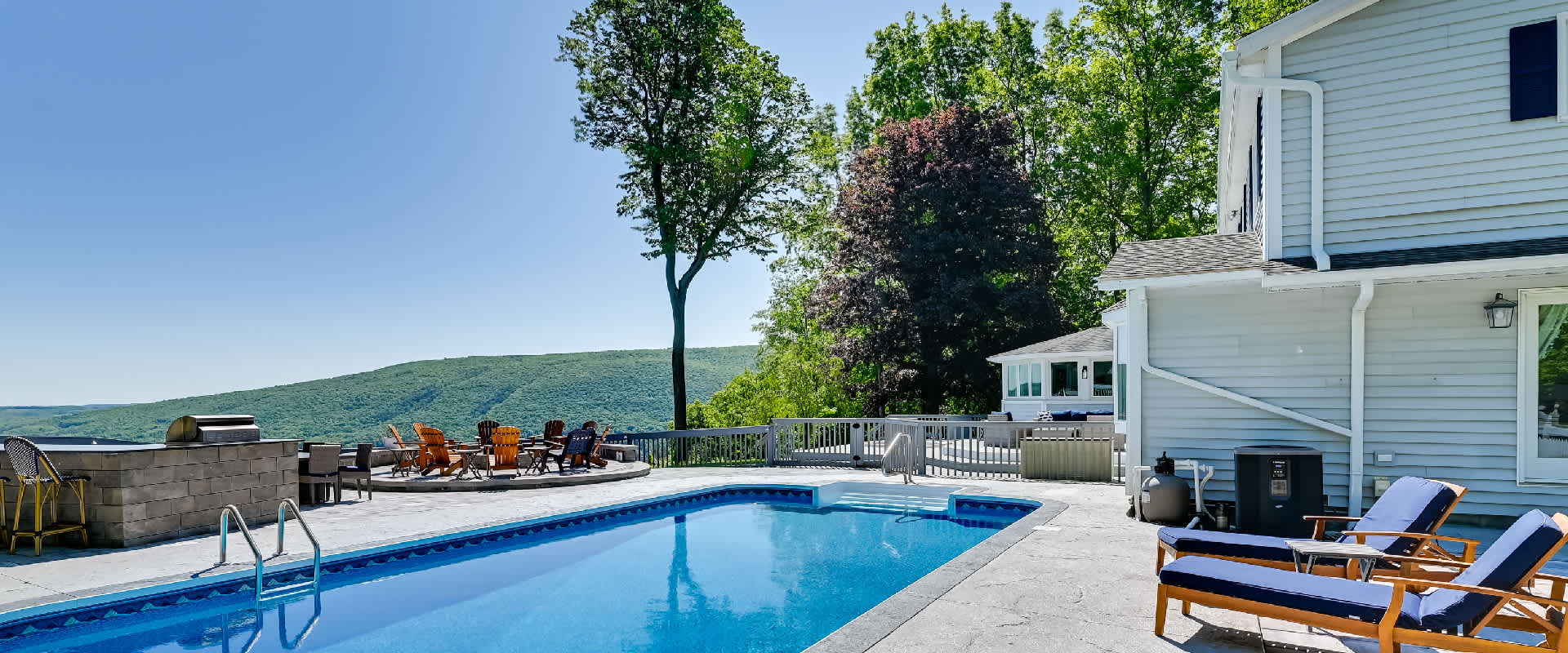 Large deck including a pool, fire pit, grill, and chairs looks out over the panoramic views of Canandaigua Lake and the surrounding hills