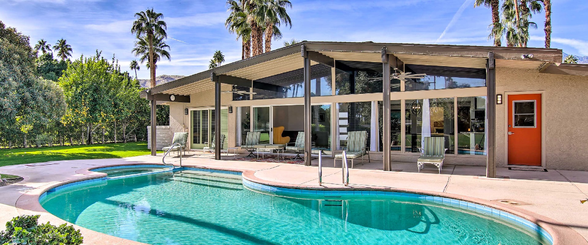 Mid-century modern home sits next to a bright outdoor pool surrounded by palm trees