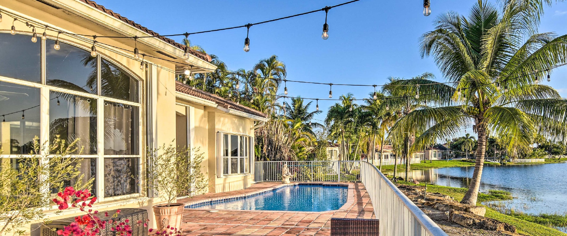 Villa with private patio and pool looking out over a lakefront, surrounded by palm trees and decorated with string lights