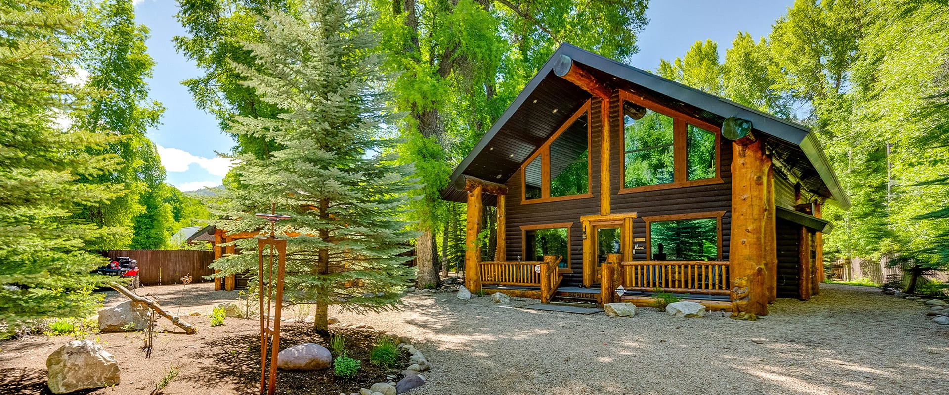 Exterior view of a modern log cabin with massive windows reflecting the towering green pines surrounding it.