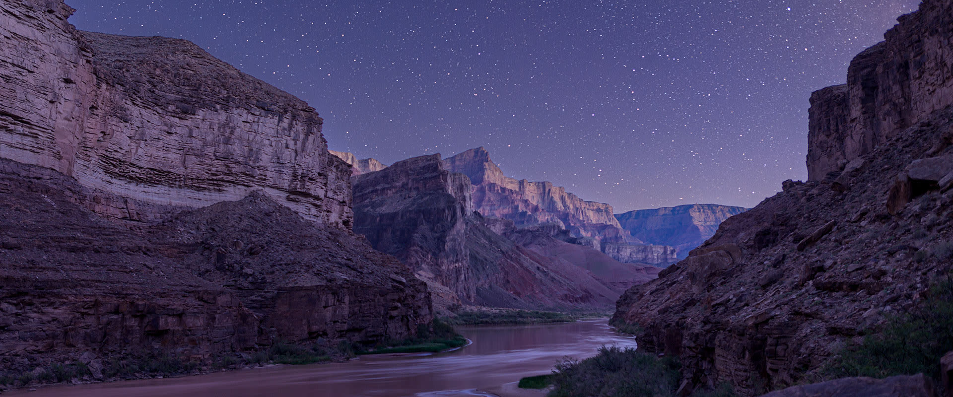 Picturesque photo of Grand Canyon National Park at night with a clear view of the stars and the Colorado River.