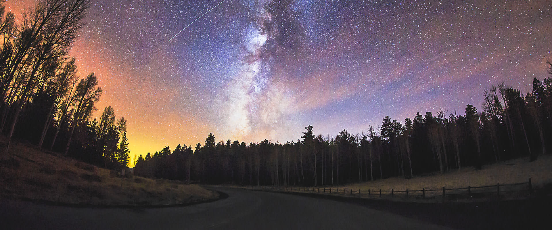 Photo of The Milky Way and stars shining brightly over a forested road near Flagstaff, Arizona.