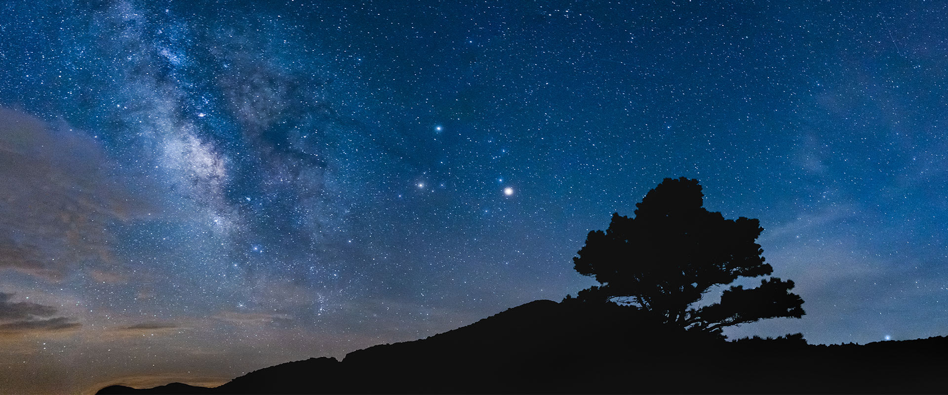 Photo of the night sky and Milky Way with Blue Ridge Mountain silhouettes in the distance near Spruce Pine, North Carolina.