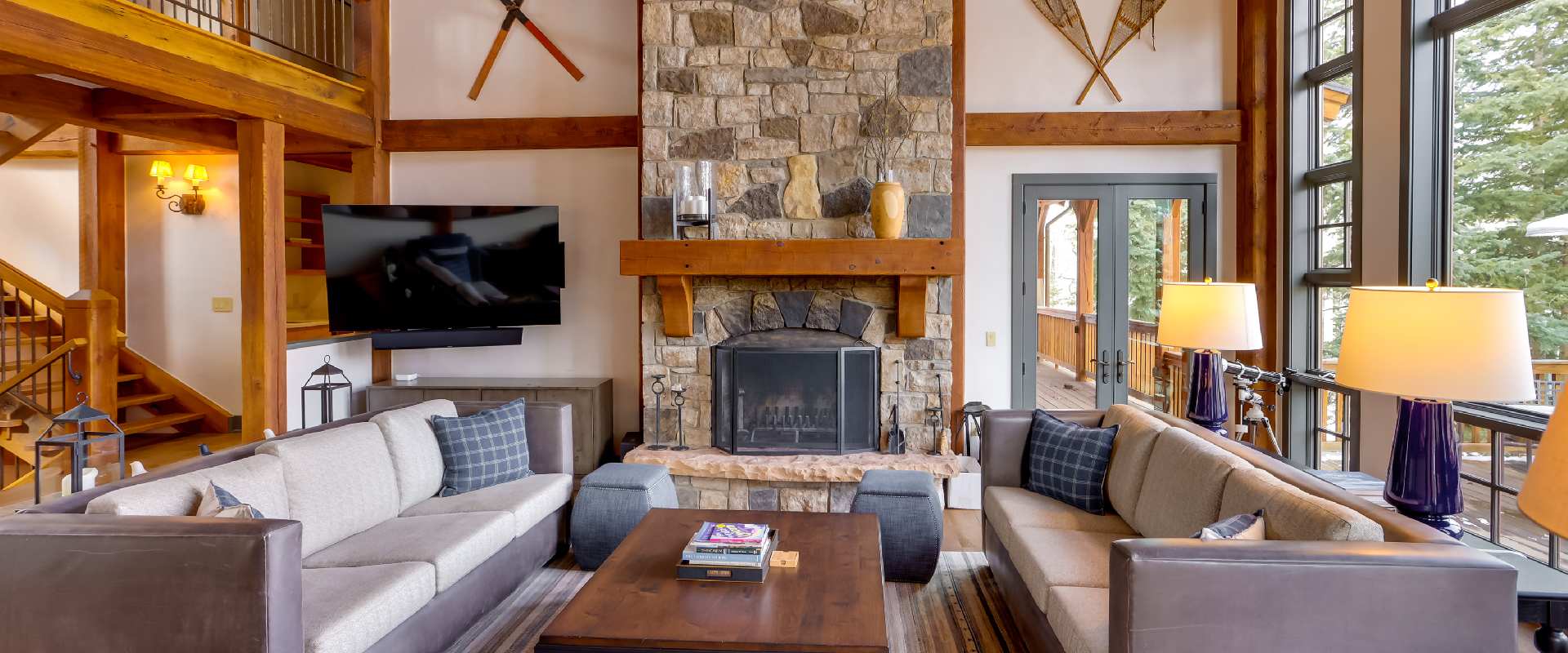 Photo of a modern cabin living room in Telluride with a stone fireplace, modular couches, a flat screen tv, and dark purple lamps. The location and amenities make it one of the top luxury vacation rentals in the U.S.
