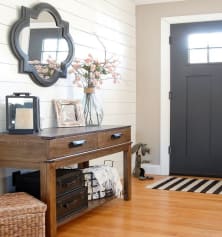 Vacation rental front entryway with shiplap accent wall, wood hallway table, decorative mirror, and floral arrangement