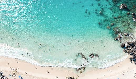Aerial view of people on shore and in the water at one of Kona Coast, Hawaii's white sand beaches
