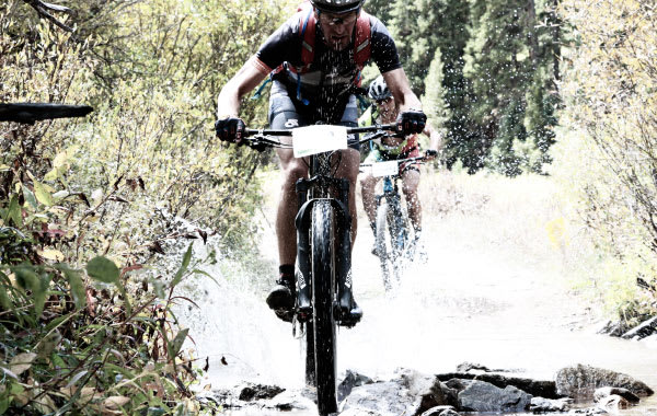 Man mountain biking through a creek in the woods