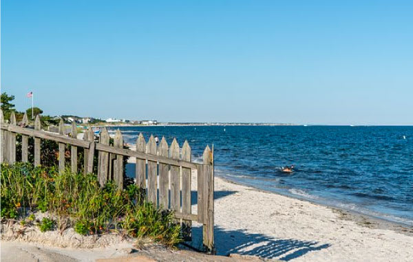 Sandy shoreline in Cape Cod, Massachusetts with brown picket fence