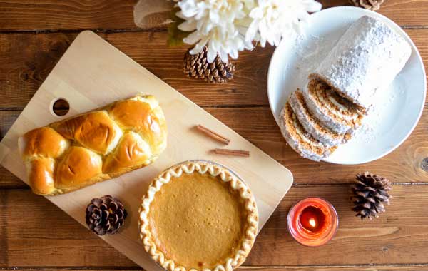 Spread of seasonal holiday treats and breads, with pinecones, candles, and flowers decorating the table