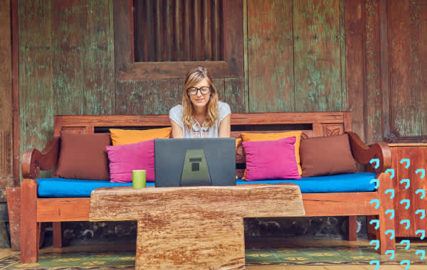 Woman sitting on a bench outside a house working on a laptop.