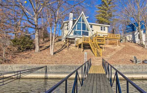 A-frame lake cabin with steps leading down to a long, narrow dock over the water