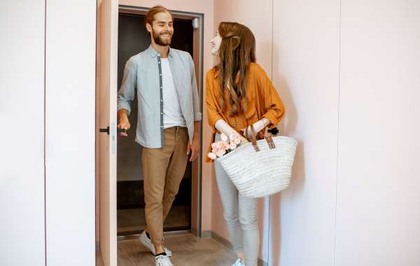 Photo of a couple walking through a door to a vacation rental property, woman holding a bag with flowers inside