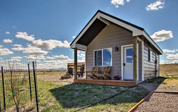 Tiny home cabin with Adirondack chairs and a fire pit, surrounded by Montana land and a bright blue sky