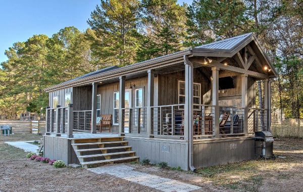 Tiny house rental in Winnsboro, TX with a furnished porch and grill, surrounded by trees