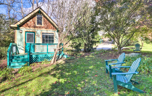 Colorful turquoise cottage surrounded by foliage and greenery with Adirondack chairs for seating