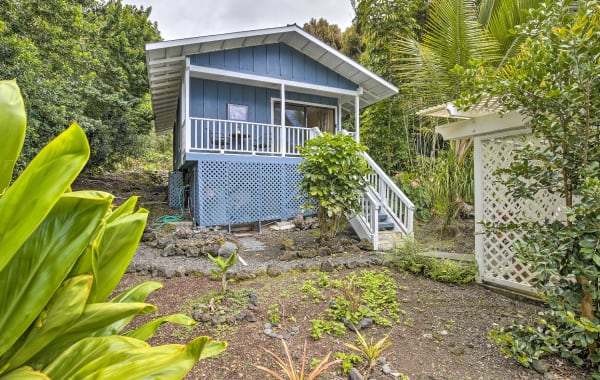 Light blue tiny house rental in Kailua-Kona, HI with an elevated front porch with stair access, surrounded by lush vegetation